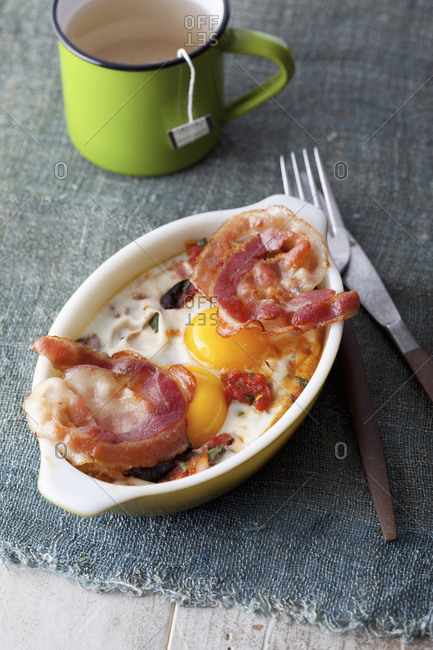 Hearty breakfast of baked eggs and bacon with a mug of tea