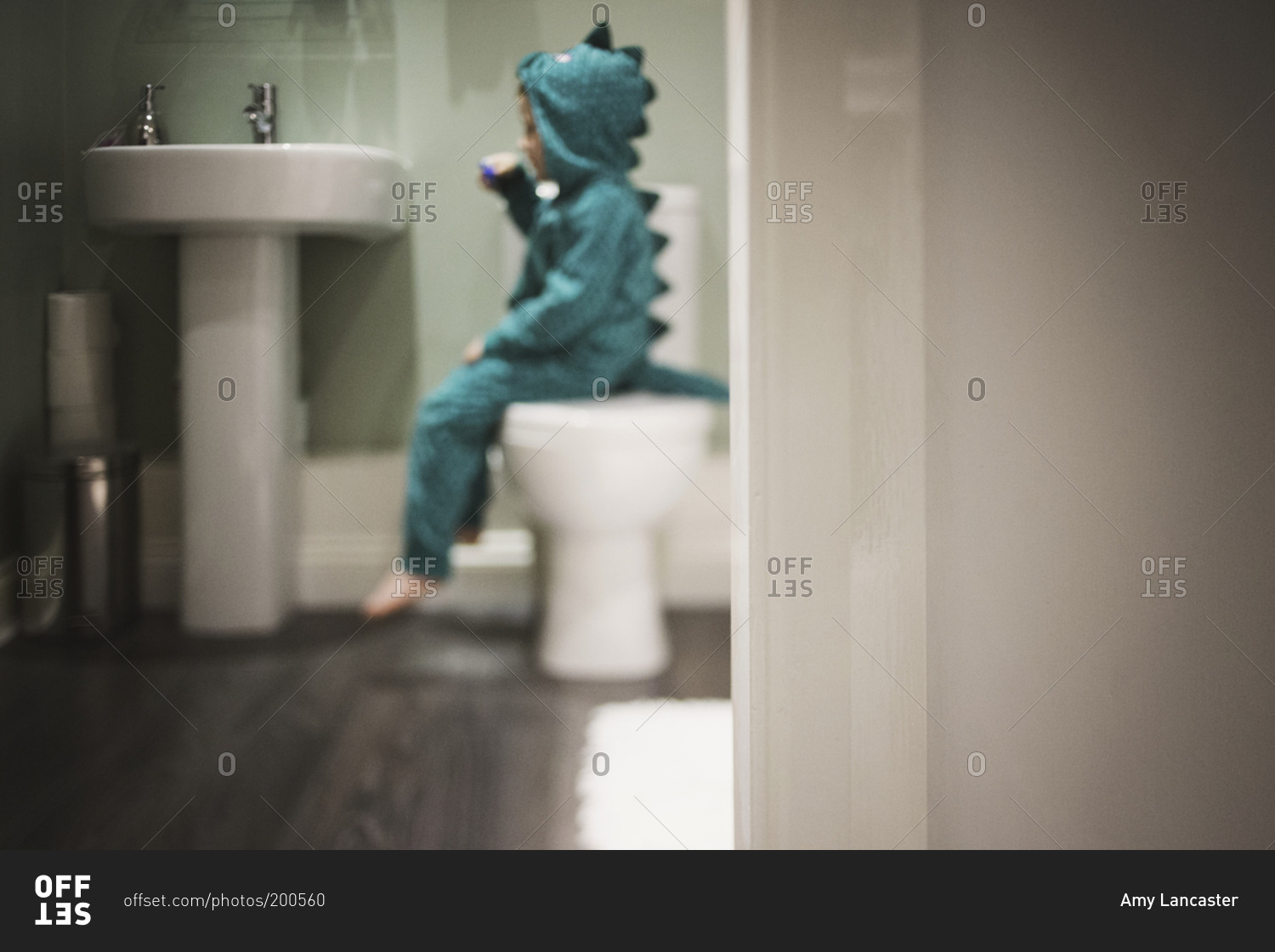 Child in dinosaur costume brushing his teeth while sitting on the toilet