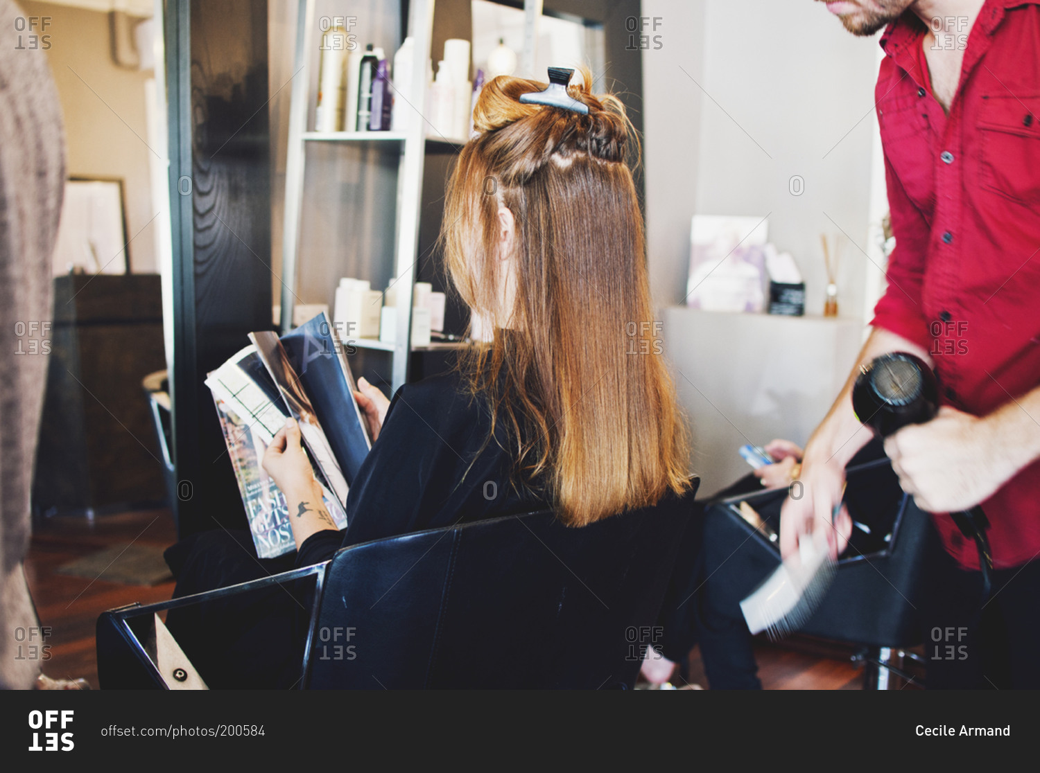 Woman reading a magazine in a salon chair while stylist dries her hair