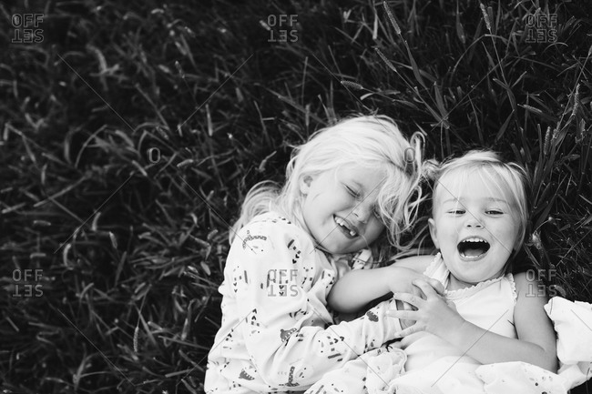 Two little girls laughing laying in grass stock photo - OFFSET