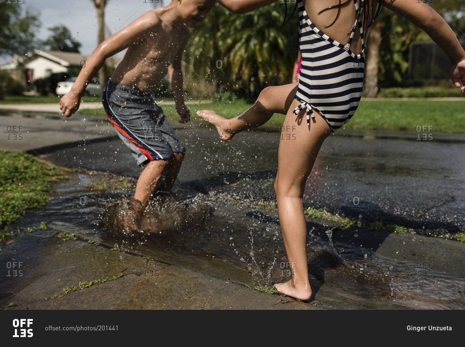 Two siblings splashing in puddle in summertime