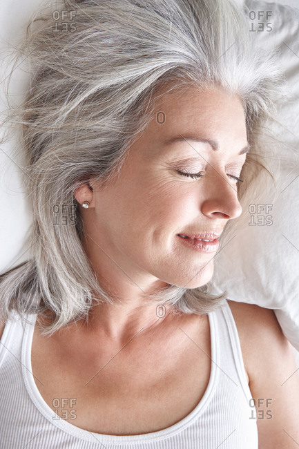 Woman with grey hair sleeping in bed smiling