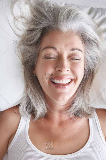 Woman with grey hair lying in bed laughing