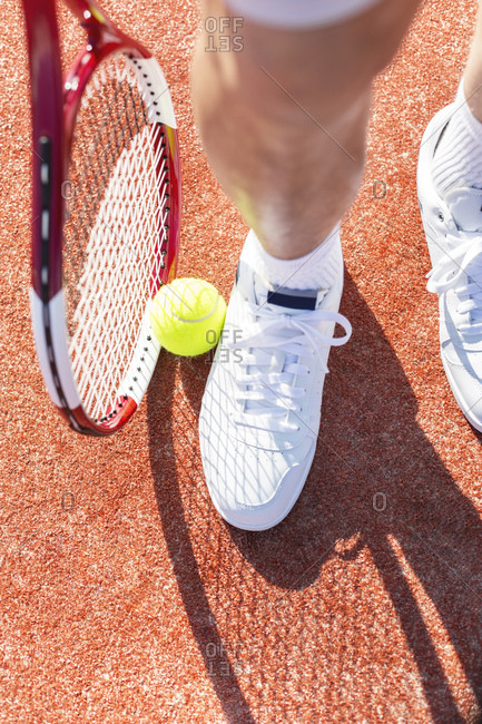 Leg of tennis player, tennis ball and racket on court