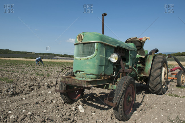 An old tractor in field with farmer working in the background