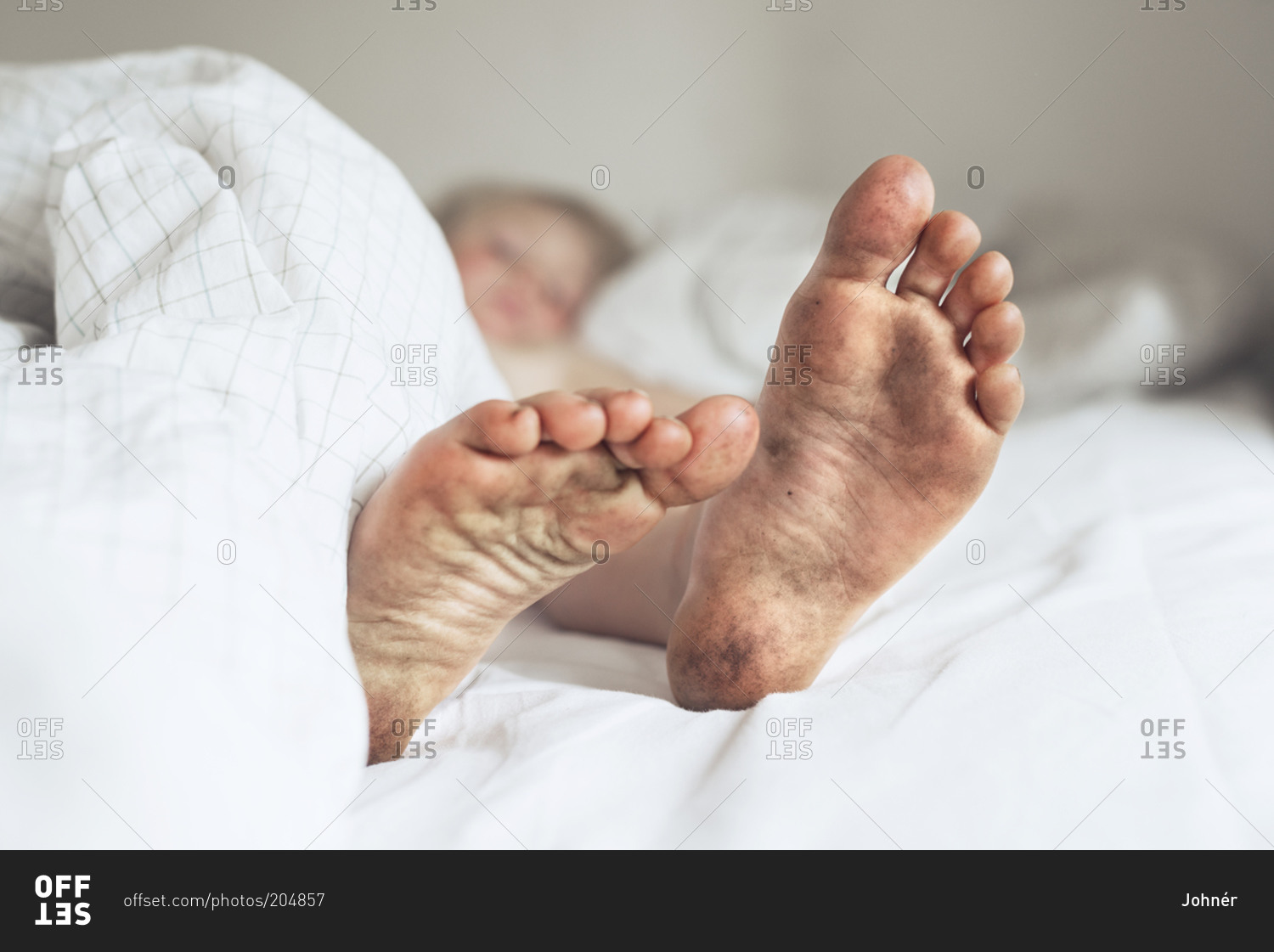 Child's dirty feet in bed stock photo OFFSET