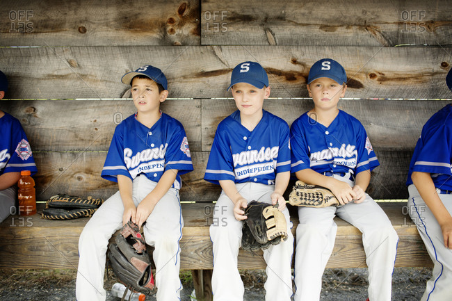 A young, black baseball player sits in the dugout during a