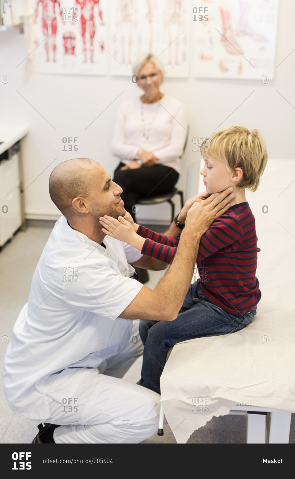 Senior woman looking at doctor while he checks boy's throat at clinic
