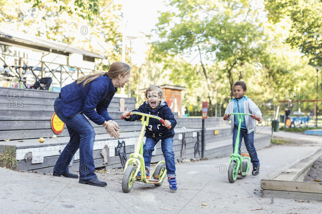 Teacher motivating children to push scooters during race