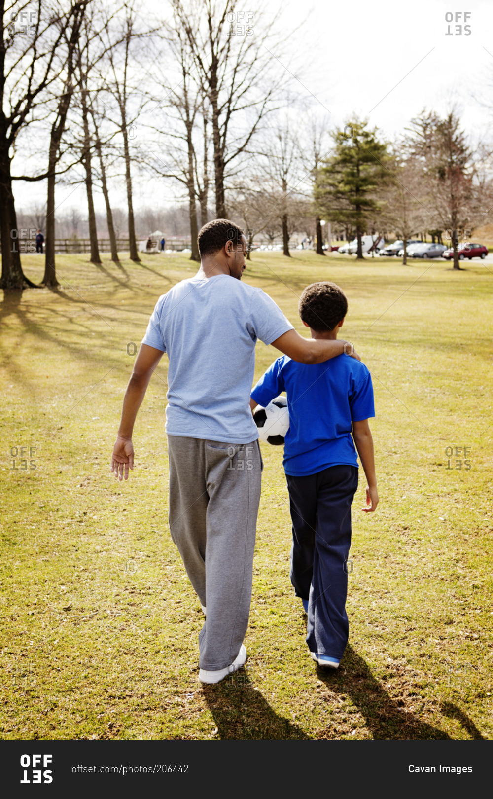 Father With Arm Around Son Walking In Park Stock Photo Offset