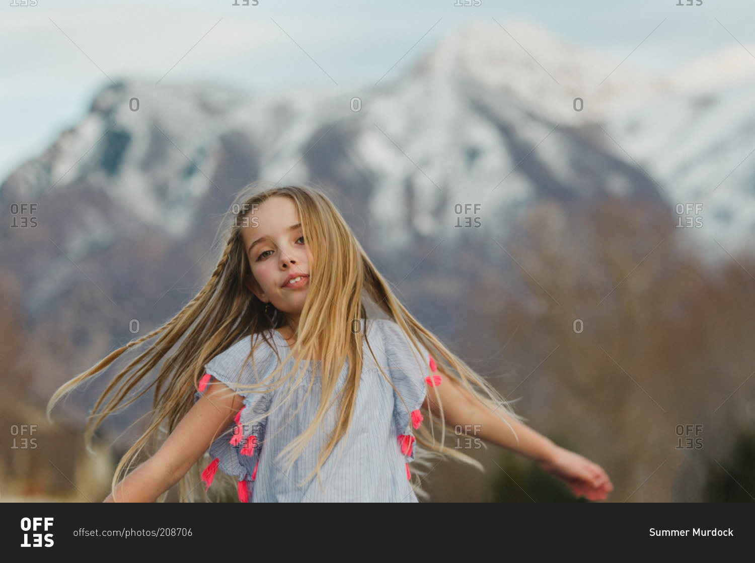A girl spins around in front of snowcapped mountains
