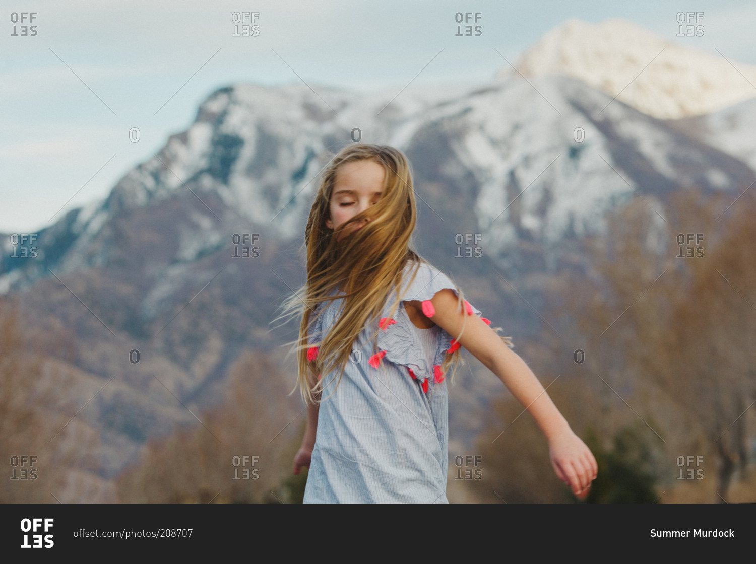A little girl spins around in front of snowcapped mountains