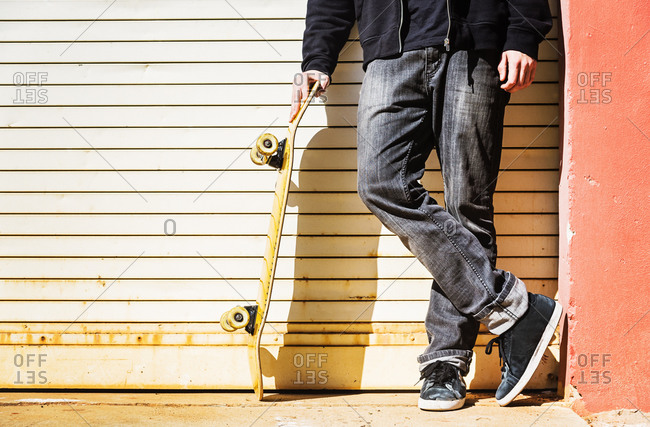 Feet of man with skateboard leaning on garage door