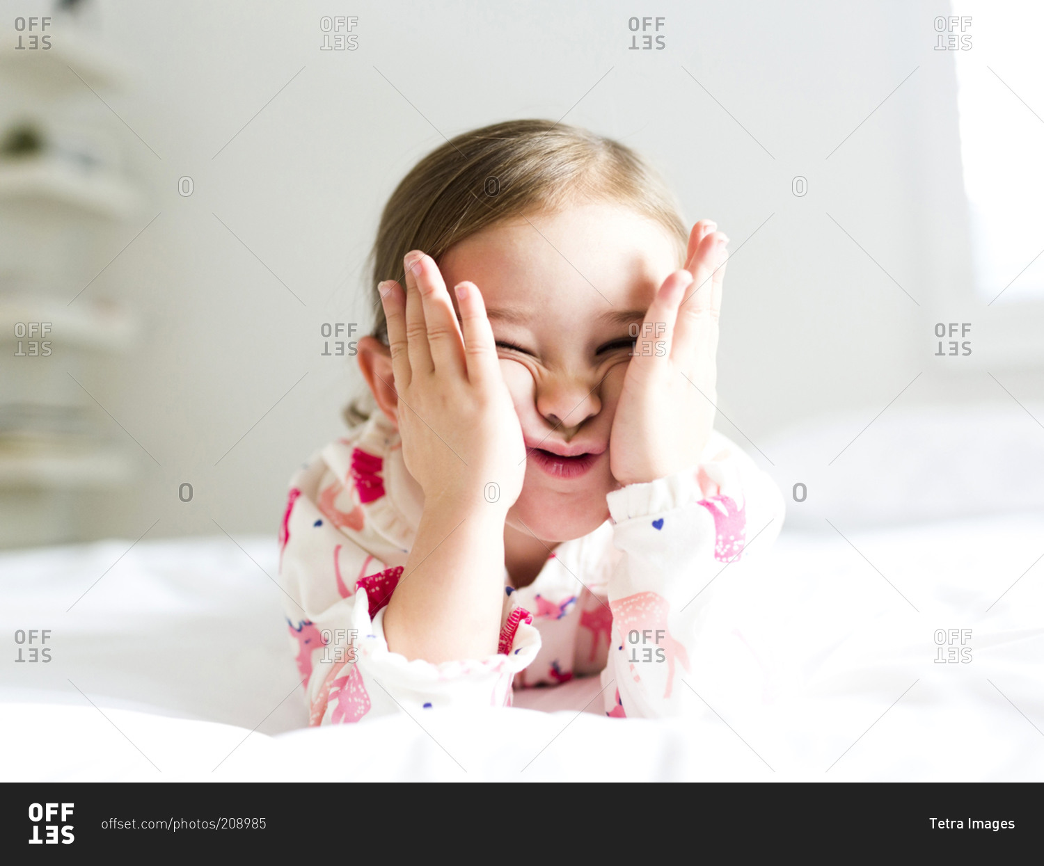 Girl lying on bed pulling funny face stock photo - OFFSET