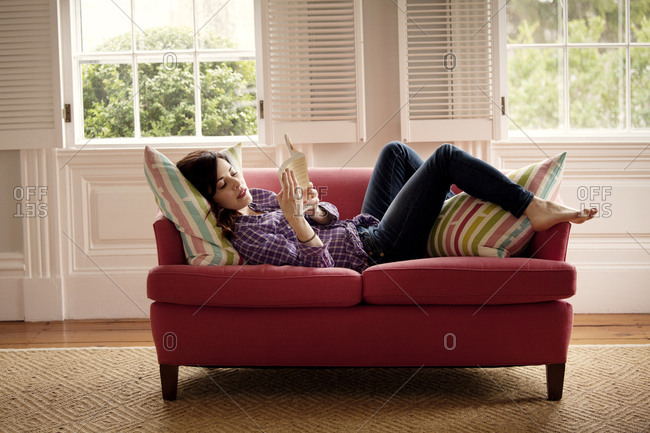 A young woman reads a book on a loveseat