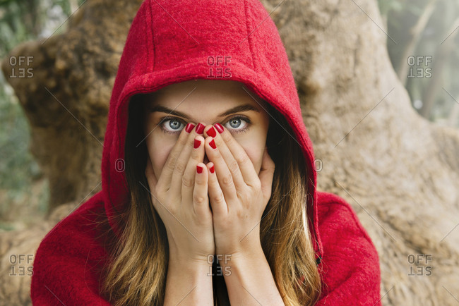 Frightened woman wearing red hood covering face with her hands