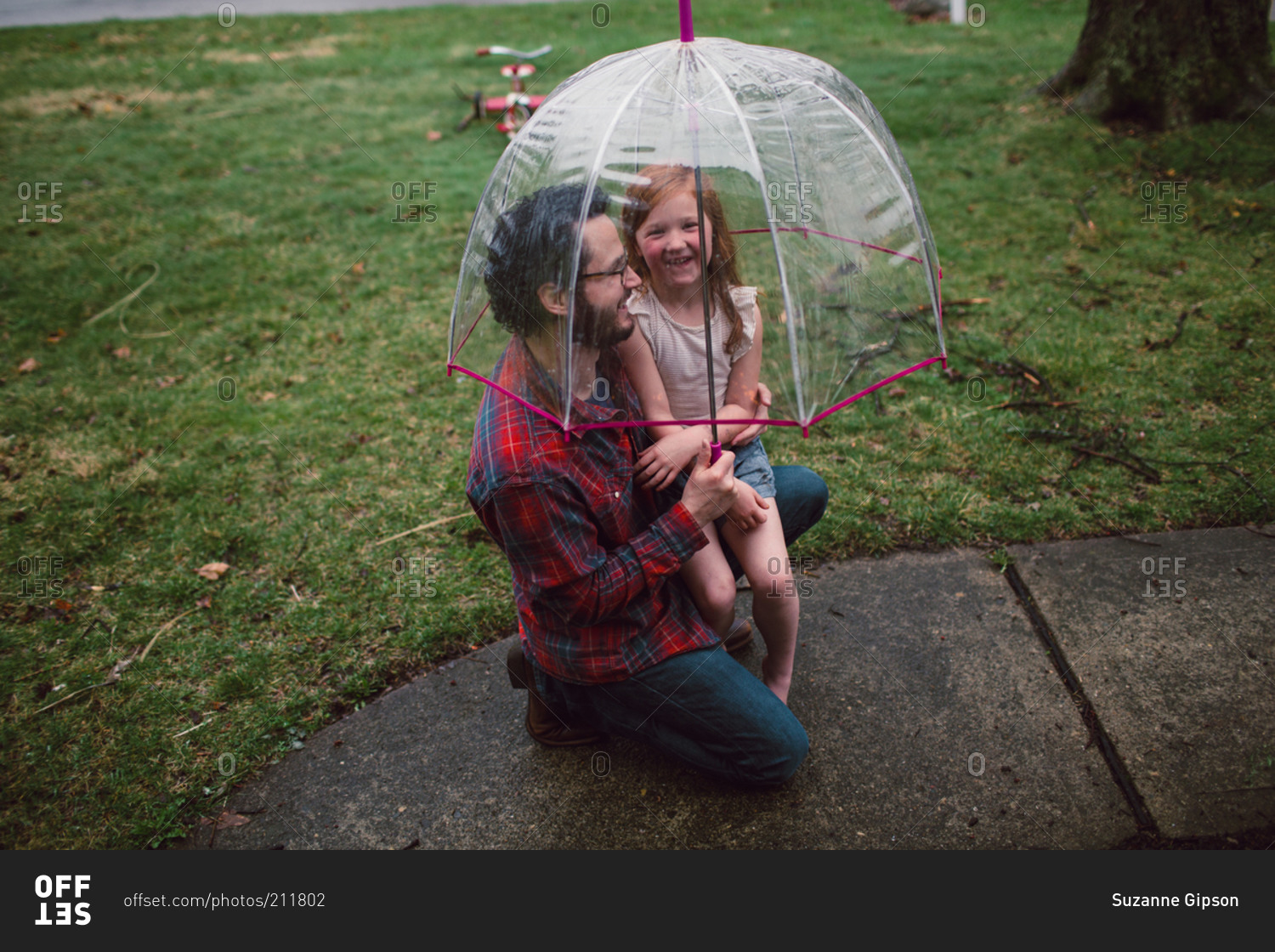 A little girl and her dad giggle under a bucket umbrella