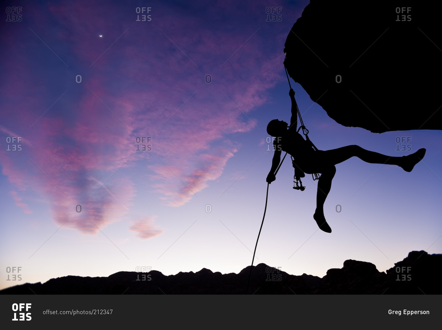 Silhouette of a climber hanging from rock face at sunset