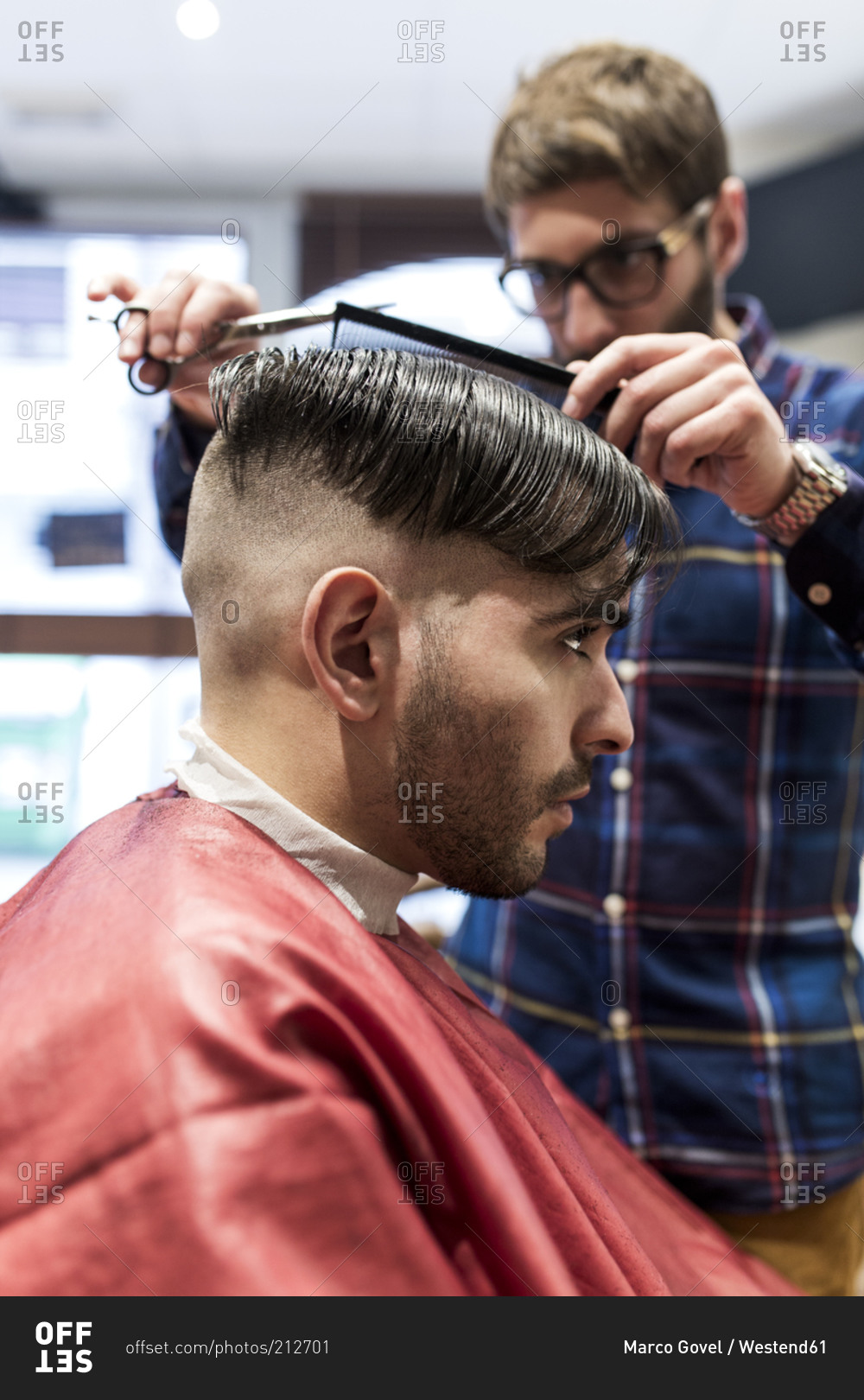 Hairdresser parting a young man's hair in a barbershop
