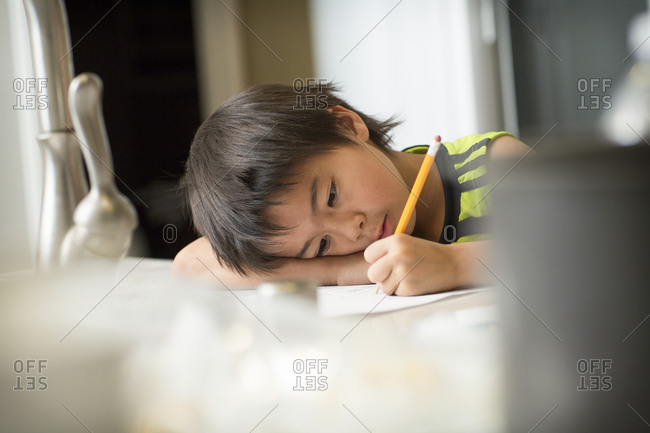 A Japanese boy tired of doing his Japanese homework in a kitchen