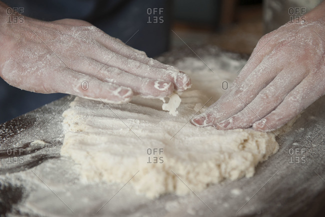 Hands patting down raw biscuit dough