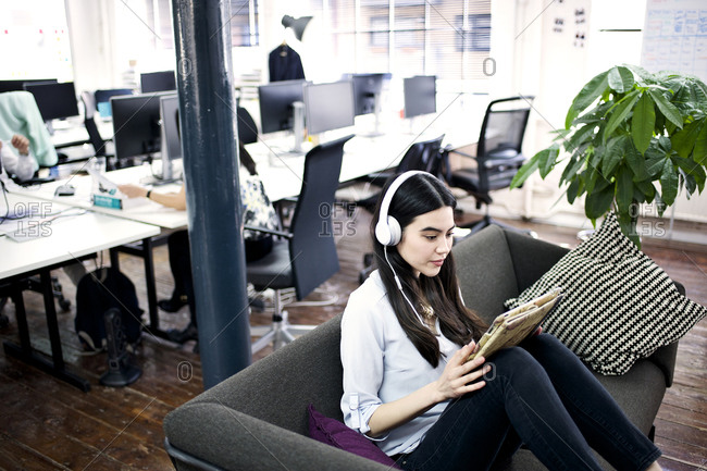 Woman on office couch with tablet, headphones
