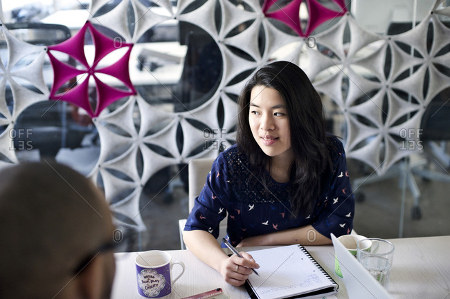 Young woman taking notes and listening in meeting