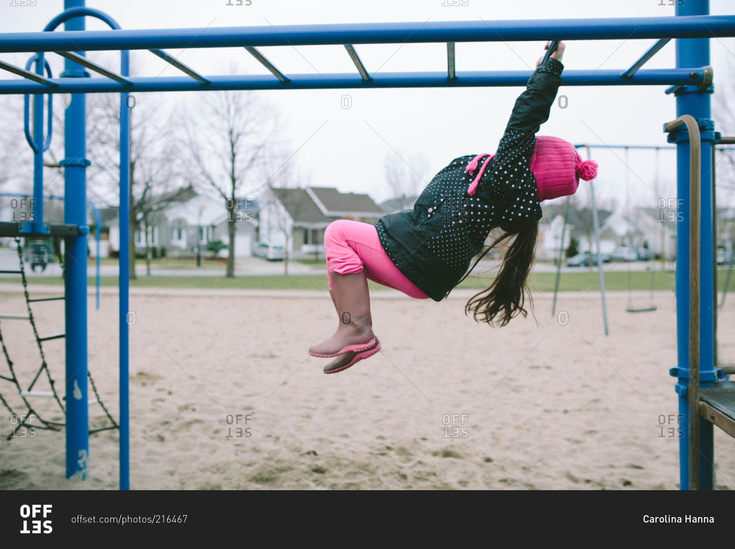 Young girl hanging from monkey bars stock photo OFFSET