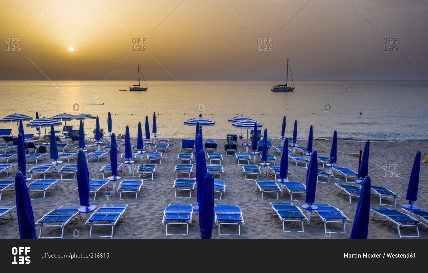 View to beach umbrellas and loungers in front of the sea at evening twilight, Cefalu, Sicily