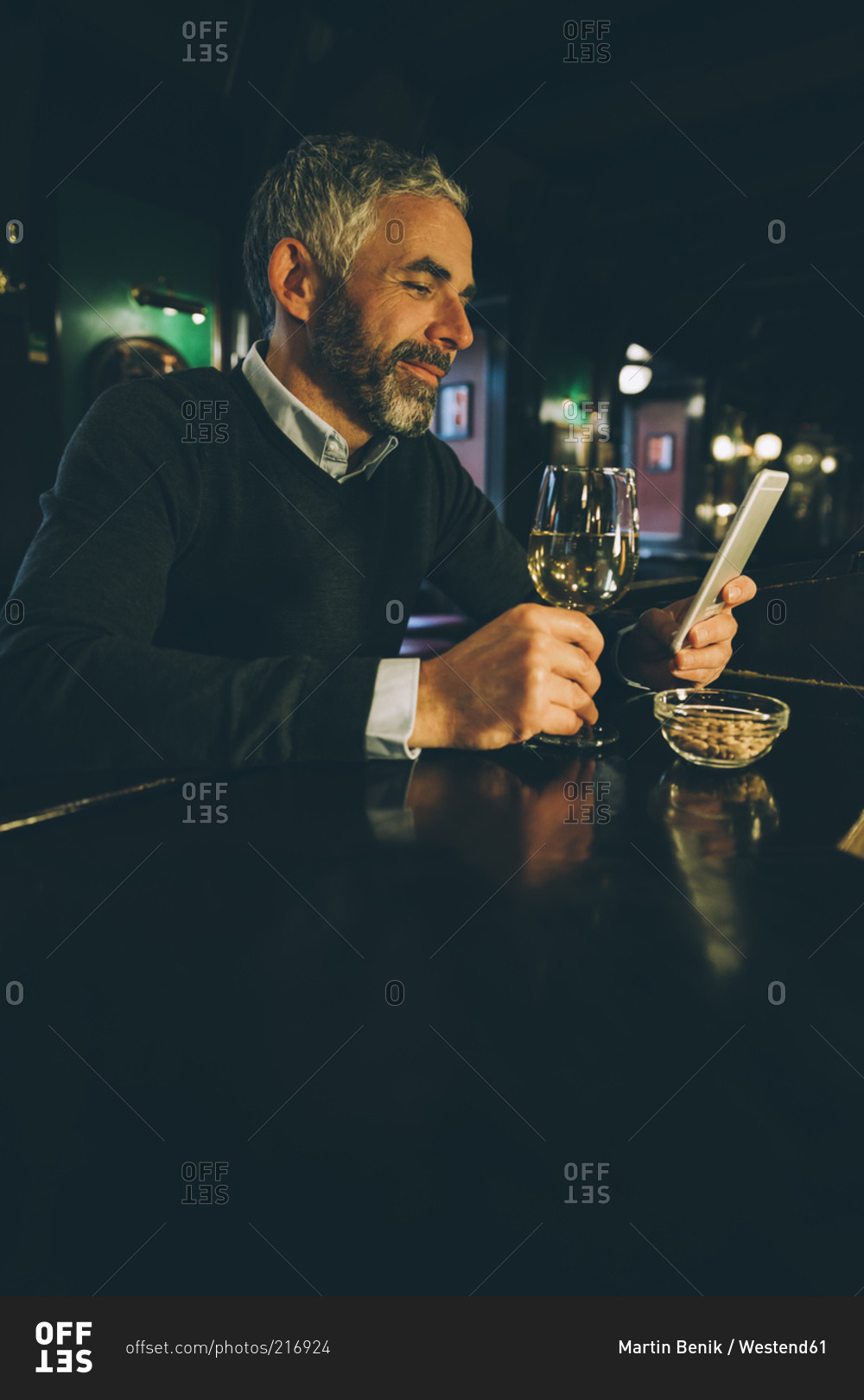 Smiling man sitting at counter of a pub using smartphone