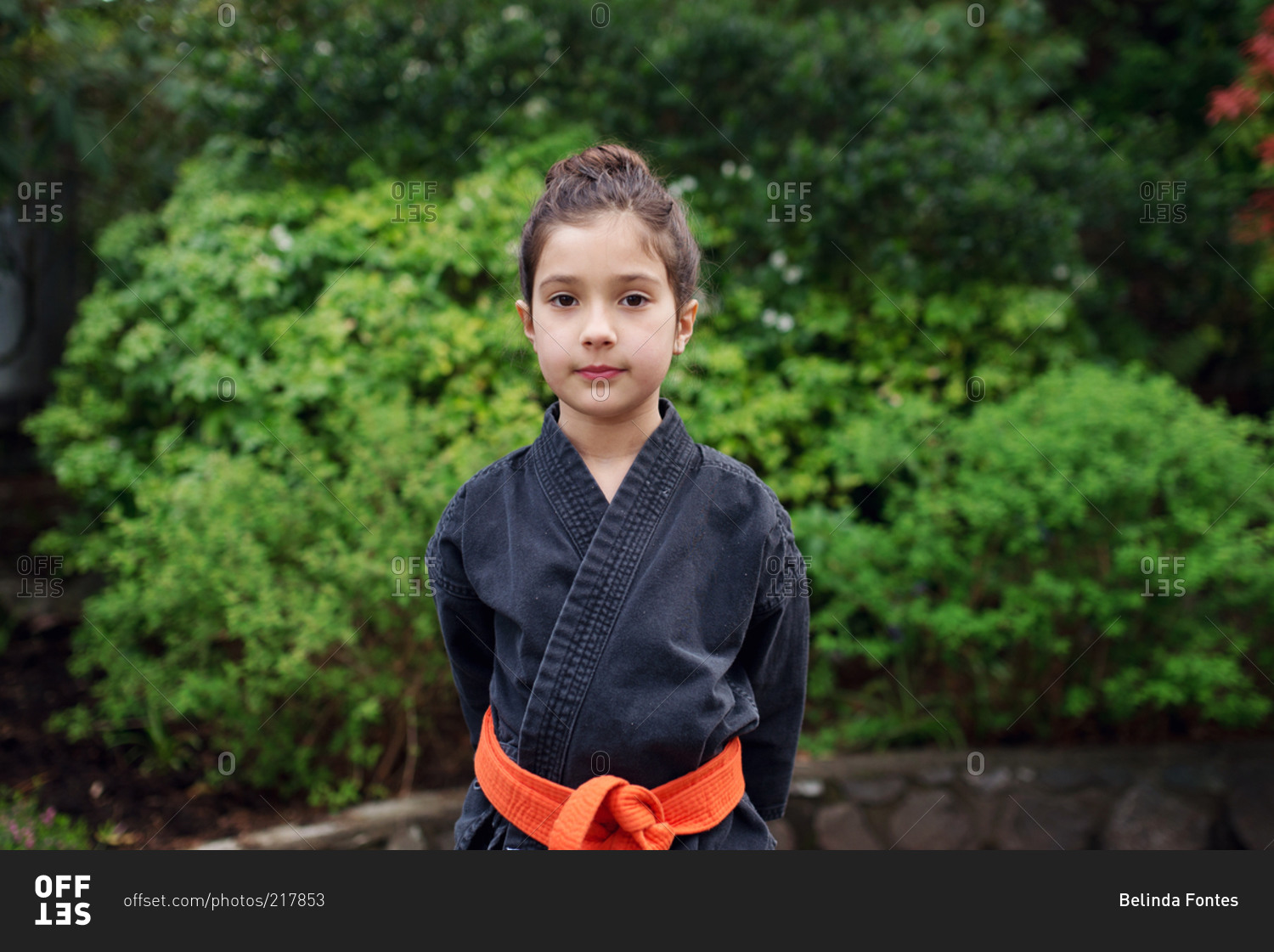 A girl in a karate outfit stands still with her hands behind her back