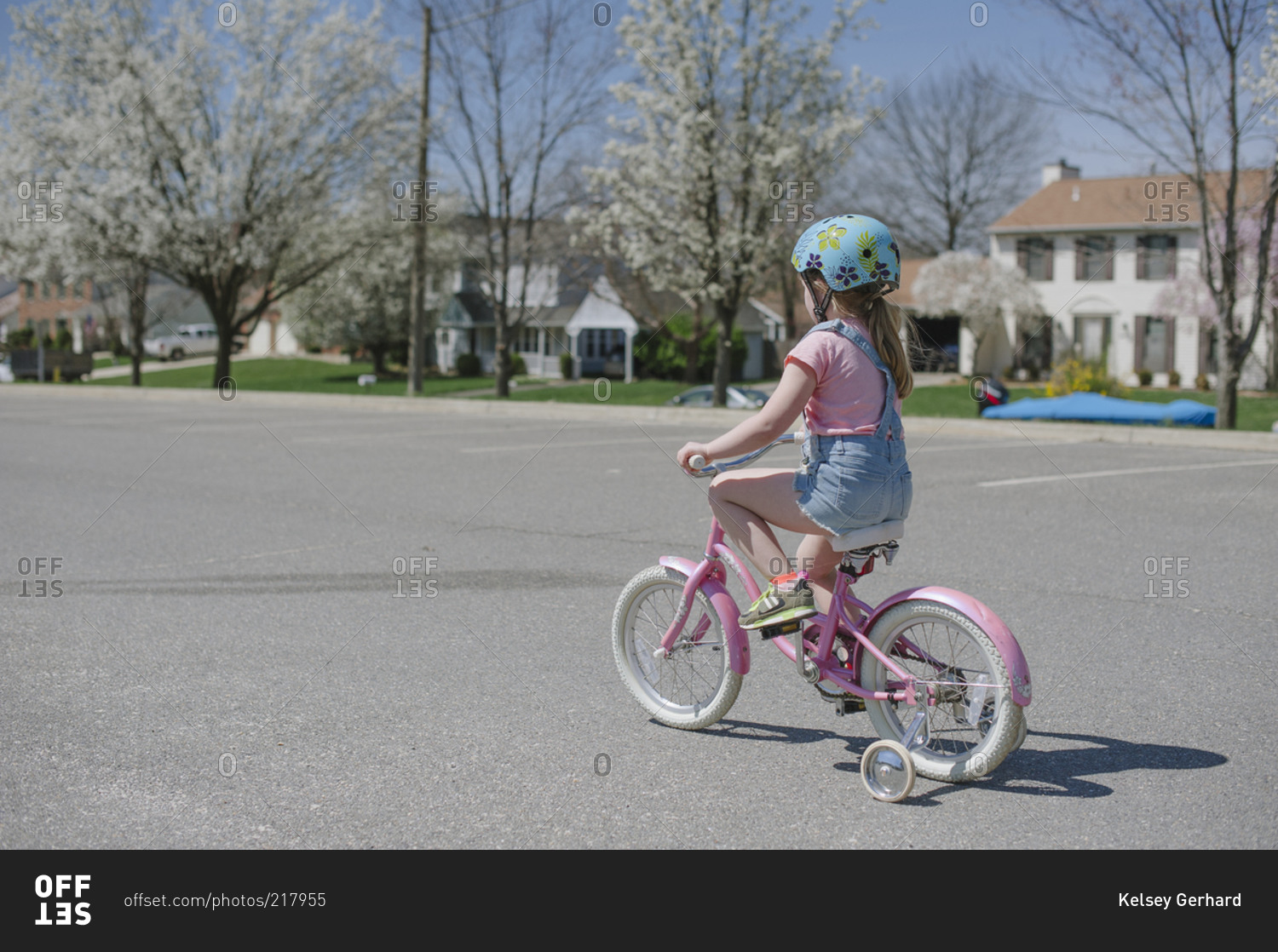 Little girl riding a pink bike with training wheels