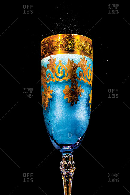 A crystal and gilt champagne flute filled with blue bubbling liquid