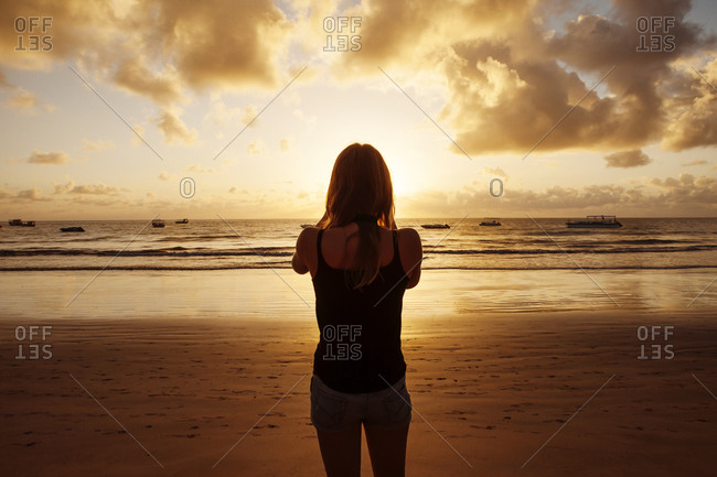 A woman stands on the beach and watches the sunset