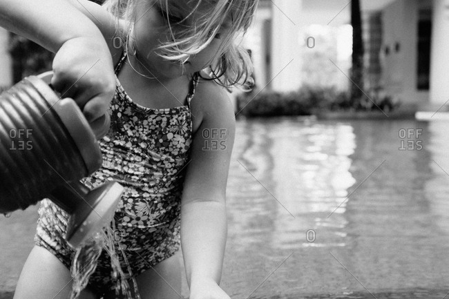 Toddler girl playing with a watering can in pool