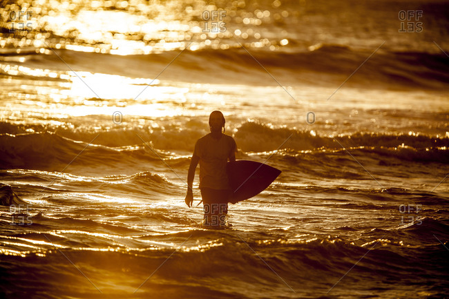 Man with surfboard at sundown, Bali