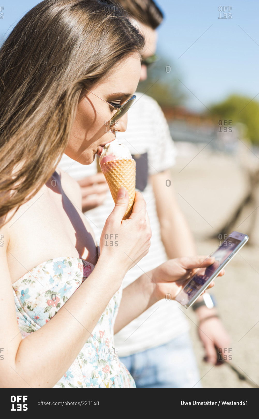 Young couple with ice cream cone and smartphone outdoors in summer