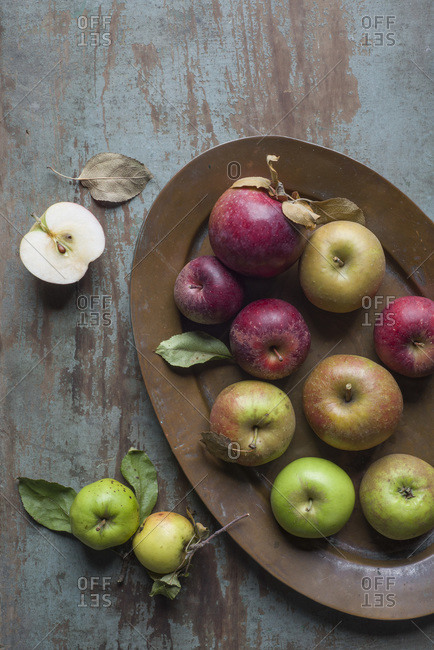 A variety of heirloom and other apple varieties on a copper tray and a rustic wooden board