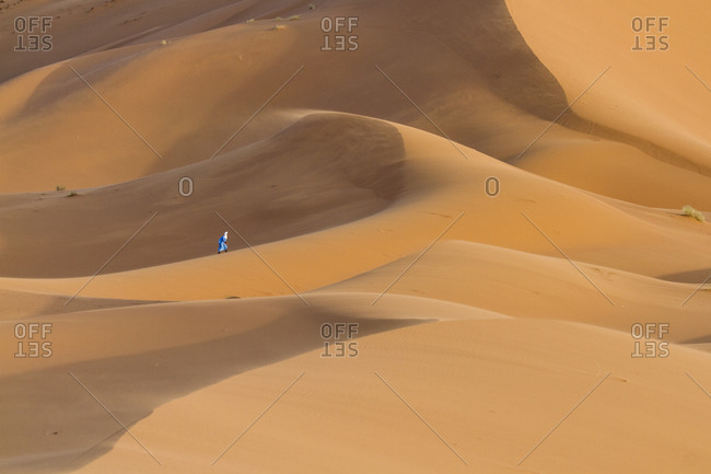 Touareg man with the typical blue dress walks alone the sahara desert Merzouga, Morocco