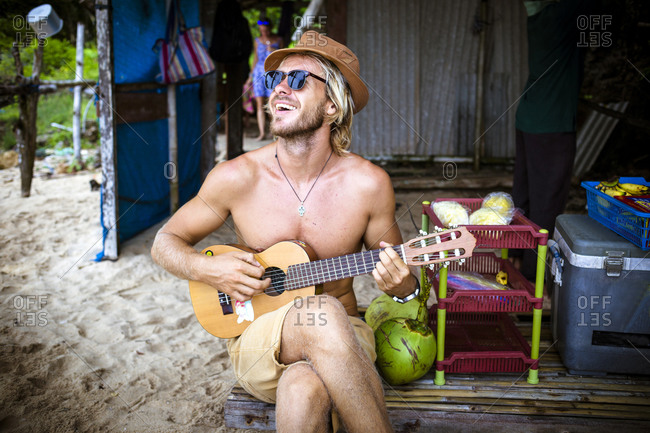 Young man playing the ukulele on the beach photo - OFFSET