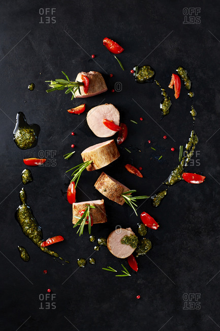 Arrangement of veal slices, basil pesto, slices of red bell pepper and red peppercorns on black background