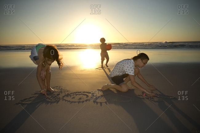 Children On The Beach At Sunset Drawing In Sand Stock Photo Offset