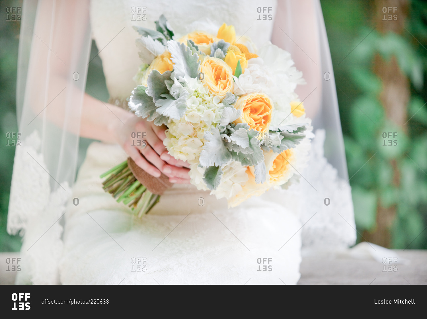 A yellow, white and silver bouquet of flowers in bride's hands