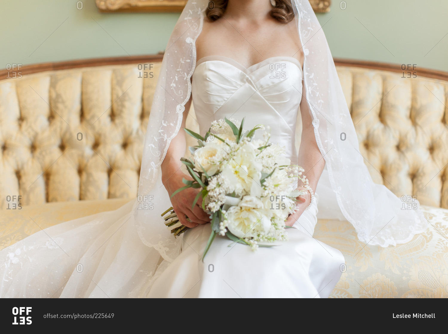 Bride wearing a lace veil and white gown seated on an elegant sofa