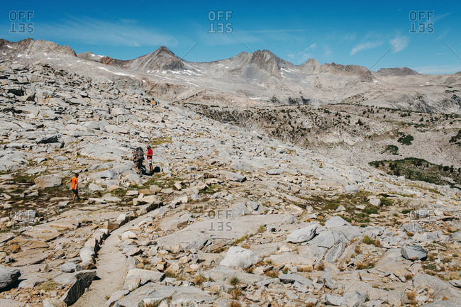 A boy and two men wander through a rocky terrain