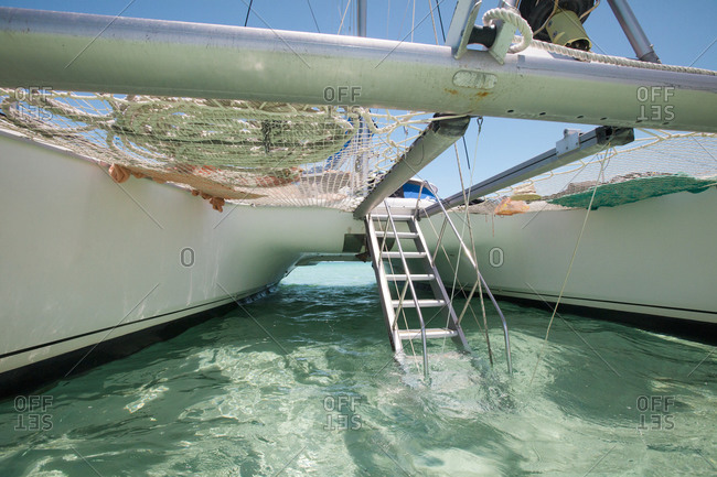 A drop-down aluminum staircase leads up to the deck of a catamaran boat