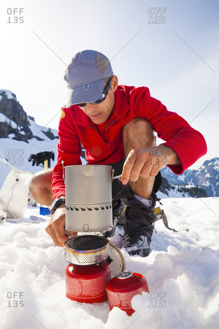 A climber uses a camping stove to make his dinner while camping in the mountains