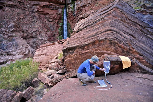 Male hiker filters water on a cliff-pinched patio near Deer Creek Falls in the Grand Canyon