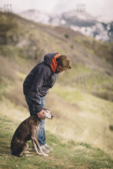 A man pets his dog on a mountain walk