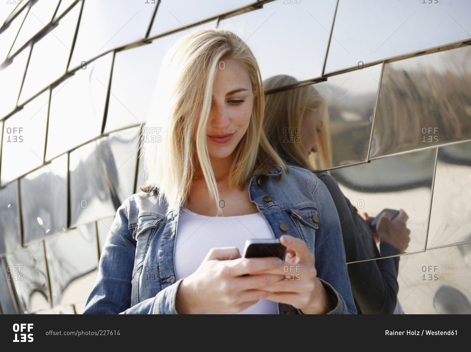 Smiling blond woman looking at her smartphone in front of modern facade